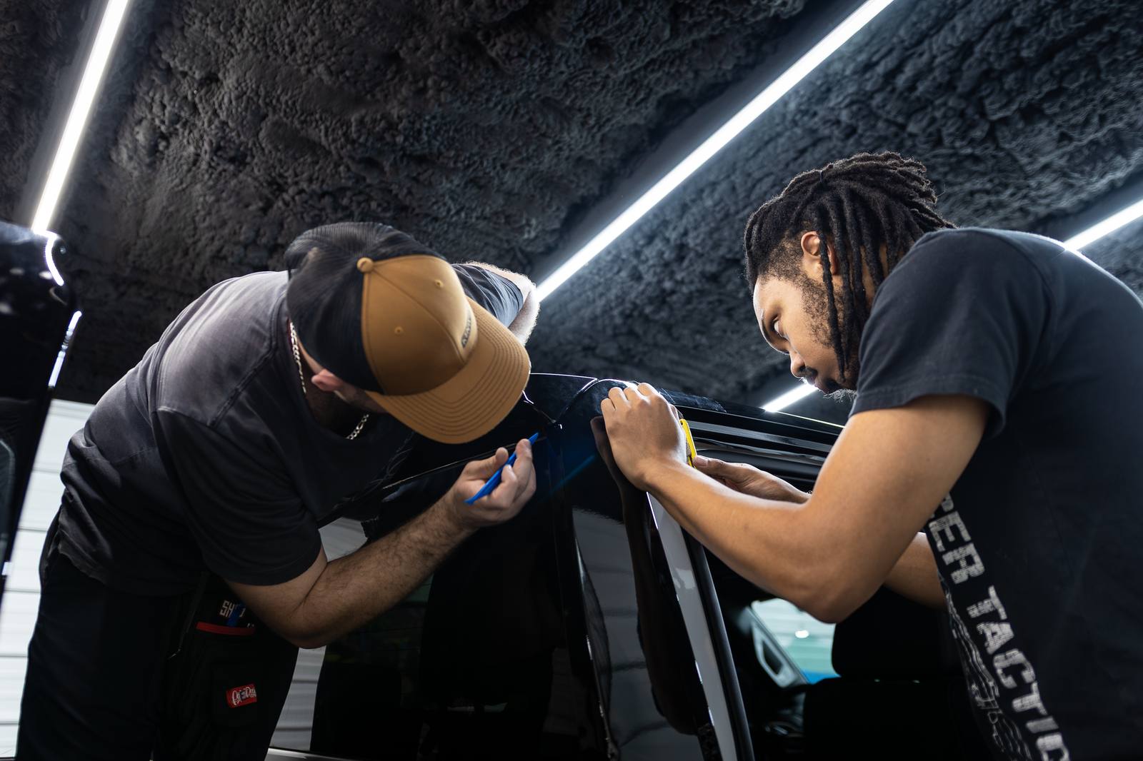 Two installers fitting film along a door edge under shop lighting