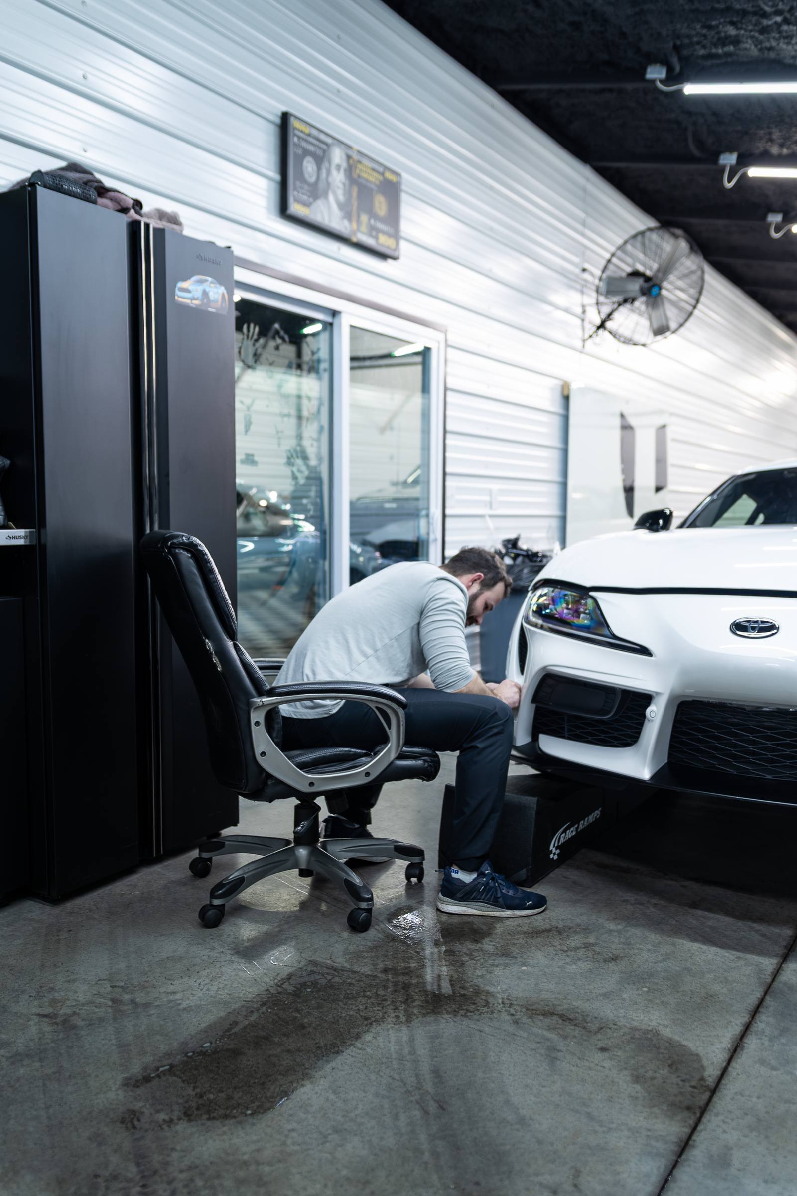 Detailer working on the front of a white sports car inside the shop